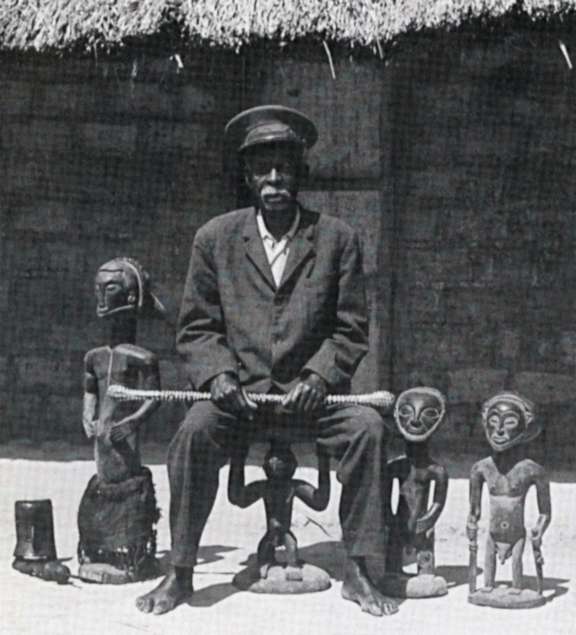 Photograph of a Hemba chief on a caryatid seat, surrounded by three lusingiti statues, circa 1970–1985. © D.R