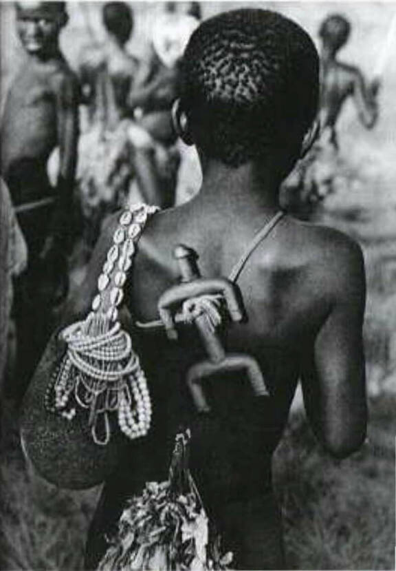 Jeune fille portant « une poupée ». Photographie d’Yves Schaller. S.d. Voir KRÜGER Christoph, "Dowayo : Namchi Puppen aus Kamerun Die Dowayo und ihr Kult", Düsseldorf, Verlag U. Gottschalk, 2003.