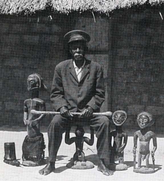 Photographie d’un chef hemba assis sur un siège à cariatide et entouré de trois statues lusingiti, vers 1970-1985. © D.R